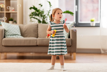 childhood and family concept - little girl blowing soap bubbles at home