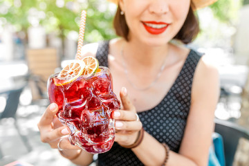 Beautiful girl drinking a red cocktail from a skull glass in cafe