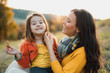 A portrait of young mother with a small daughter in autumn nature at sunset.