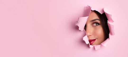 beauty salon advertising banner with copy space. beautiful girl looks through hole in pink paper bac