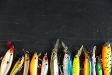 Various Of Fishing Lures Colorful On Black Stone Wet Background.