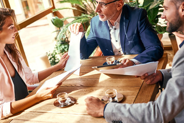 Business lunch. Three people in the restaurant sitting at table brainstorming working on project while senior man searching information on digital tablet close-up