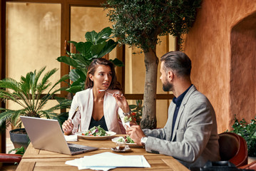 Wall Mural - Business lunch. Man and woman sitting at table at restaurant eating healthy fresh salad discussing project