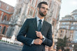 © Friends Stock - Close up profile portrait of a successful young bearded guy in suit and glasses. So stylish and nerdy. Outdoors on a sunny street, fixing his cuffs