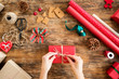 DIY Gift Wrapping. Woman wrapping beautiful red christmas gifts on rustic wooden table. Overhead point of view of christmas wrapping station.