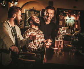 Wall Mural - Old friends having fun and drinking draft beer at bar counter in pub.