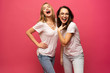 © opolja - Two exited woman having fun and raising hands up. Standing on pink background. Lucky mood.
