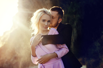 Man and a woman hugging in the summer at sunset in beautiful clothes. Couple in love stands on the shore on the rocks in the sun, hugging and kissing in the splashes of water. Pink dress