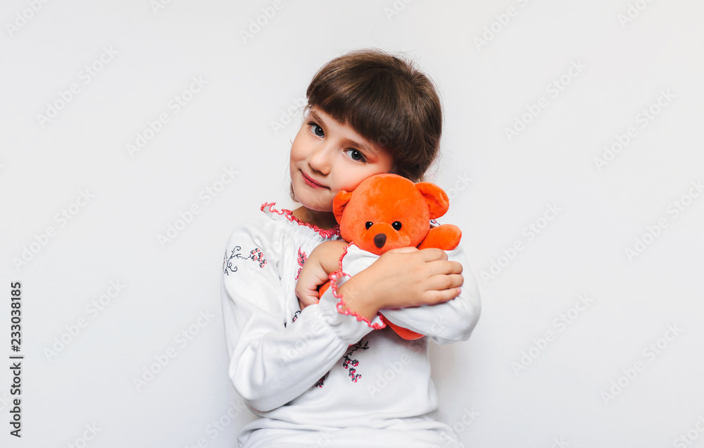 A little girl is hugging a soft orange teddy bear on a white background ...