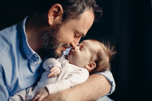 Closeup Portrait Of Middle Age Bearded Caucasian Father Hugging And Kissing Newborn Baby. Male Man Parent Holding Child. Authentic Lifestyle Touching Tender Moment. Single Dad Family Life Concept.