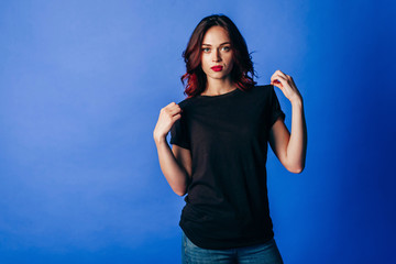 Beautiful young girl in posing in black t-shirt in the studio on blue background. Space for your logo