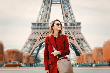 Wall Mural - Style redhead girl in red coat and bag at parisian street in autumn season time. Eiffel tower on background