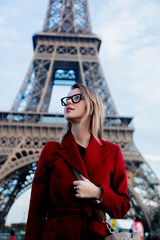 Style redhead girl in red coat and bag at parisian street with view at Eiffel tower in autumn season time