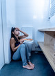 © SB Arts Media - Young beautiful bulimic woman sitting on the bathroom floor eating pizza looking guilty