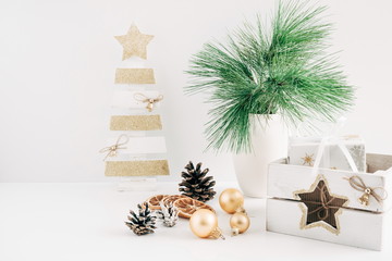 Home Decor, Interior. Decorative wooden Christmas tree, vase with fir branches, cones, Christmas decorations, gift on a white table. 