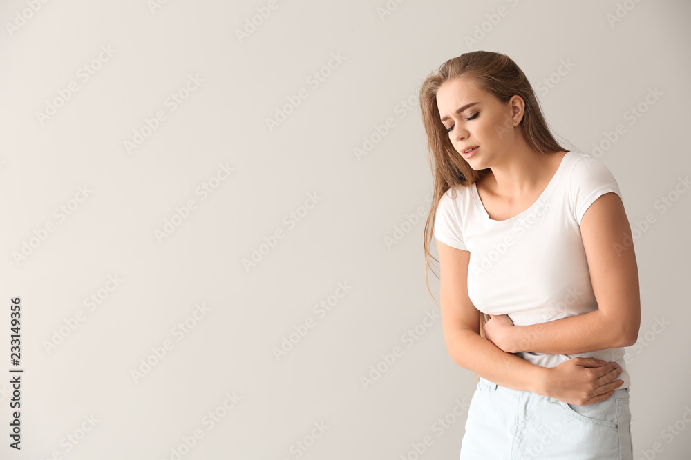 Young woman suffering from abdominal pain on light background - obrazy, fototapety, plakaty 
