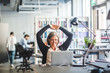 © Maskot - Smiling businesswoman looking at laptop while sitting in office