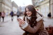 © Dusan Petkovic - Cute young girl in winter coat standing in street and looking at her telephone. Smiling and looking happy.