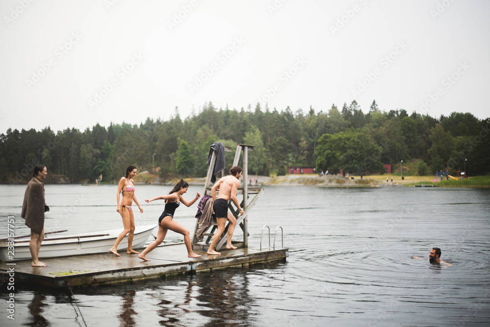 Carefree male and female friends running on jetty for diving in lake ...