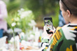 © Maskot - Cropped image of woman photographing dining table through mobile phone in backyard