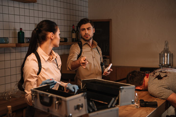 Wall Mural - focused female and male detectives using evidence collection kit and investigating dead body at crime scene together