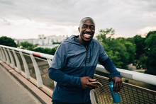 Portrait of smiling athlete holding smartphone and bottle while standing outdoors