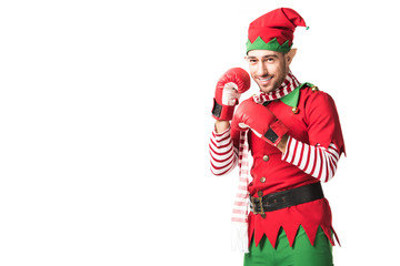 Wall Mural - smiling man in christmas elf costume wearing red boxing gloves and looking at camera isolated on white