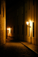 Old Lanterns Illuminating A Dark Alleyway Medieval Street At Night In Prague, Czech Republic. Low Key Photo With Brown Yellow Tones From The Lanterns As Single Light Sources Against The Dark Shadows