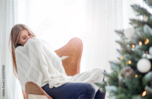 Fotografia Young relaxed woman sitting on armchair and resting near Christmas tree