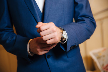 Wall Mural - Close-up man puts on a gold watch with a leather belt, businessman is dressed in a stylish suit, a white shirt.