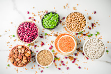 Various Assortment Of Legumes - Beans, Soy Beans, Chickpeas, Lentils, Green Peas. Healthy Eating Concept. Vegetable Proteins. White Marble Background Copy Space Top View