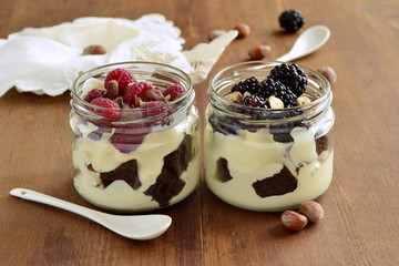 Wall Mural - Dessert with chocolate biscuit, cream, hazelnut and fresh berries in glass jars, trifle