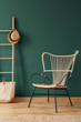 © Photographee.eu - Rattan armchair next to bag and hat on ladder in green living room interior with rug. Real photo