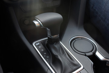 car interior indoor. black leather automatic gearbox with chrome button and sun rays, round ashtray