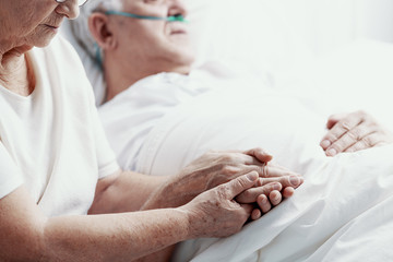 Wall Mural - Senior man with lung cancer laying in hospice bed supporting by his elderly wife, photo with copy space