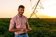 © Zoran Zeremski - Young farmer holding tablet in his hands and adjusts irrigation system on soybean field at sunset.