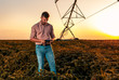 © Zoran Zeremski - Young farmer holding tablet in his hands and adjusts irrigation system on soybean field at sunset.