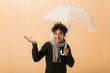 © Drobot Dean - Portrait of teenage african american guy wearing sweater and scarf standing under umbrella, isolated over beige background