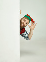 Wall Mural - The happy smiling friendly man dressed like a funny gnome or elf posing on an isolated gray studio background. The winter, holiday, christmas concept