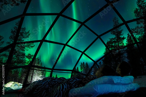 Cuadros en Lienzo CLOSE UP Young Caucasian tourist couple observing the night sky from a cool glass house in the Scandinavian wilderness