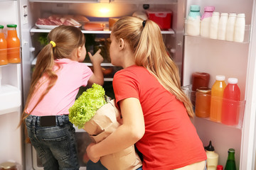 Sticker - Young mother and daughter with paper bag full of food near refrigerator at home