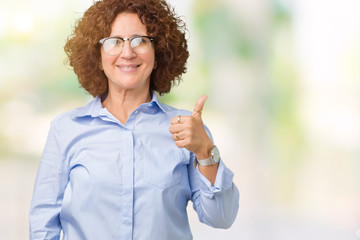 Beautiful middle ager senior businees woman wearing glasses over isolated background doing happy thumbs up gesture with hand. Approving expression looking at the camera showing success.