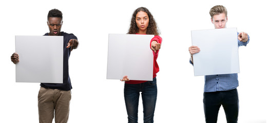 Sticker - Composition of young people holding blank banner over isolated background pointing with finger to the camera and to you, hand sign, positive and confident gesture from the front