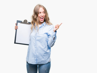 Poster - Beautiful young blonde business woman holding clipboard over isolated background very happy pointing with hand and finger to the side