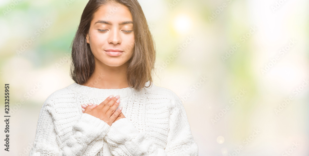 Young beautiful arab woman wearing winter sweater over isolated background smiling with hands on chest with closed eyes and grateful gesture on face. Health concept. - obrazy, fototapety, plakaty 