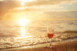 Romantic beach scene: glass of red wine at sunset near water line