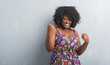 © Krakenimages.com - Young african american woman over grey grunge wall wearing colorful dress very happy and excited doing winner gesture with arms raised, smiling and screaming for success. Celebration concept.