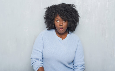 Poster - Young african american woman over grey grunge wall wearing winter sweater afraid and shocked with surprise expression, fear and excited face.