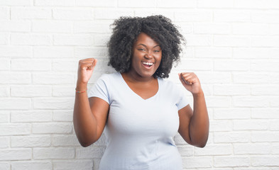 Poster - Young african american plus size woman over white brick wall celebrating surprised and amazed for success with arms raised and open eyes. Winner concept.