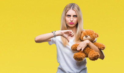 Canvas Print - Young beautiful blonde woman holding teddy bear over isolated background with angry face, negative sign showing dislike with thumbs down, rejection concept